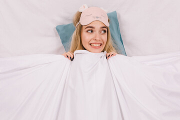 Winsome girl in sleep mask lying on pillow during photoshoot. Indoor shot of good-humoured lady spending morning in bed.