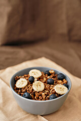 Close up of homemade granola in a plate with nuts, honey, blueberries, banana and other natural ingredients served on napkin over brown background