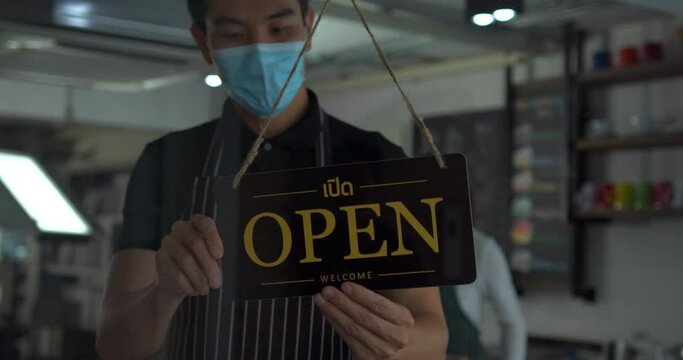 Asian man business owner in safety mask hanging up sign with inscription closed on cafe door. Waitress in protective mask closing restaurant because of pandemic.