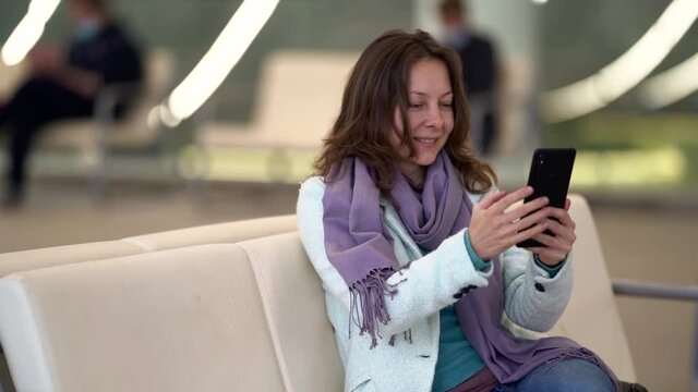 female passenger is resting in lounge area in airport, chatting online by smartphone