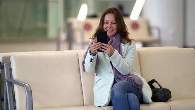 woman is waiting boarding in terminal of international airport, using smartphone with free wifi