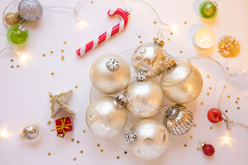 Decorated table with white table cloth, group of silver Christmas ornaments, decorative tiny gold stars, a candy cane shaped Christmas ornament, a tiny white tree with a gift, and a tea candle.