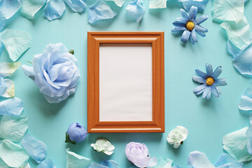 青を基調とした造花と背景。中央に縦長の木製フォトフレームの中に白いコピースペース。平置きの俯瞰撮影。