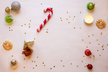White Christmas decorations background with space for text.  Decorative tiny gold stars, a candy cane shaped Christmas ornament, a tiny white tree, a tea candle and other small Christmas ornaments.