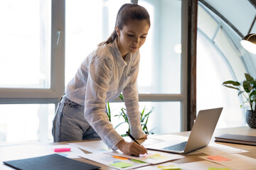 Thoughtful focused young businesswoman developing financial project on office table, preparing...