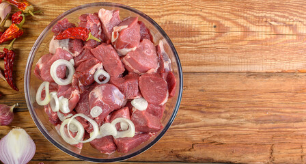 Boneless lamb steak cut into pieces, meat in a glass bowl on a wooden table, top view.