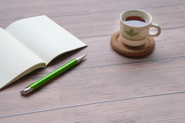 Coffee, open notepad and pen on wood table.