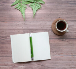 Open notepad with pen, coffee and green plants on wood table.