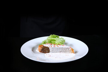 Salmon in creamy caviar sauce on a white plate. Lettuce leaves. Photo on a black background. Ready dish in a white plate.