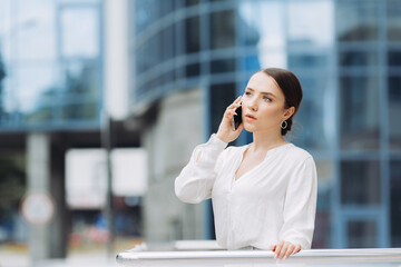 A business woman walking down the street in a business district talking on the phone.