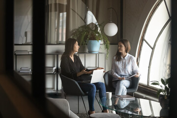 Multiethnic team of two young females enterpreneurs partners spending time at modern office or...