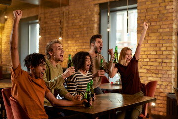 Happy friends in the bar watching sports match on TV together, drinking beer and cheering for team. People, leisure, friendship and entertainment concept