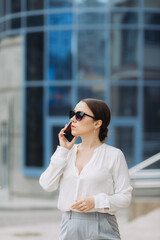 A business woman walking down the street in a business district talking on the phone.