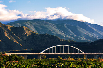 Obraz premium Viaduct of the A7 as it passes through Granada over a field of fruit trees with mountains with clouds on top.