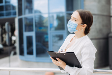 business woman wearing protection mask a holding paper holder in the business district