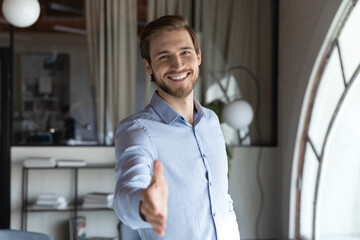 Portrait of happy young male hr stretching hand inviting you spectator to join corporate team, friendly capable manager looking at camera extending hand for handshake welcoming new client or colleague