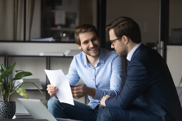 Friendly elder male employee mentor leader explaining paperwork to younger newbie colleague intern...
