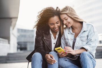 Young women friends using smartphone in a city, Cute smiling girls having fun using mobile phone on street, People, technology, friendship, relationship, mobile app, lifestyle, social media concept