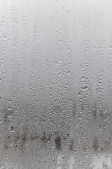 Natural drops of water flow down the glass, high humidity in the room, condensation on the glass window. Neutral colors. Vertical photo orientation