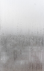 Natural drops of water flow down the glass, high humidity in the room, condensation on the glass window. Neutral colors. Vertical photo orientation