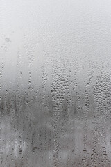 Natural drops of water flow down the glass, high humidity in the room, condensation on the glass window. Neutral colors. Vertical photo orientation