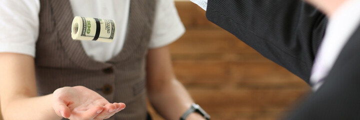 Young office manager standing opposite her chief and catching roll of money for preparing business conference