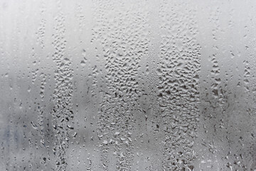 Natural drops of water flow down the glass, high humidity in the room, condensation on the glass window. Neutral colors. Excellent background with condensation drops texture