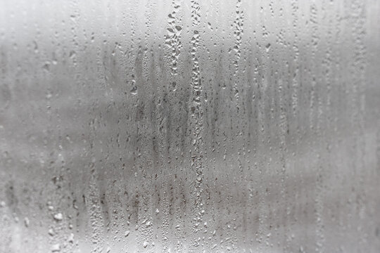 Natural drops of water flow down the glass, high humidity in the room, condensation on the glass window. Neutral colors. Excellent background with condensation drops texture