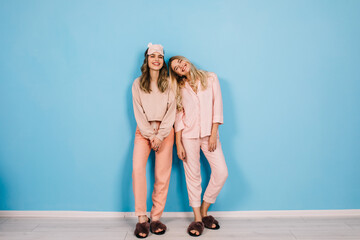 Full length view of women in pajamas standing on blue background. Young ladies posing in weekend morning.