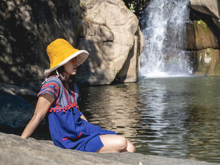 Women wear traditional Thai costumes and yellow hats. Sitting by the waterfall