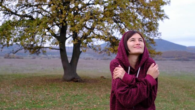 Beautiful asian woman wear deep red hood at the field by the oak in cold autumn day