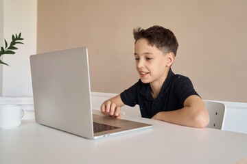 Schoolboy boy sitting at a desk with a laptop, writes school lessons during homework. High quality photo