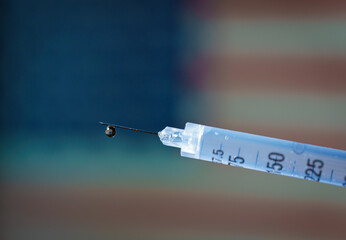 Close-up of a syringe with the United States flag waving on the background . Suitable for concepts such as covid vaccine, diabetes or drug abuse problem