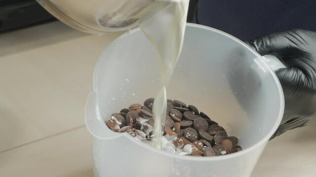a pastry chef pours hot milk into a container with chocolate tablets for making chocolate glaze. Mixing hot milk with confectionery chocolate in drops