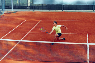 Young handsome man playing tennis on the tennis court