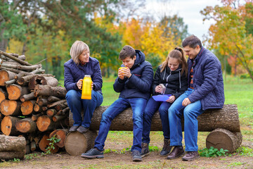 family relaxing outdoor in autumn city park, happy people together, parents and children, they drink tea and eat sandwiches, talking and smiling, beautiful nature