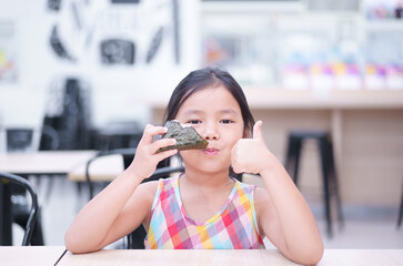 Asian child cute or kid girl enjoy eating rice ball or seaweed roll and thumbs up for japanese food...