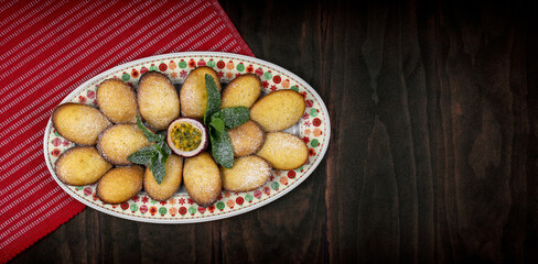 Freshly baked madeleines with a passion fruit and mint on a Christmas themed plater. The madeleines are sprinkled with icing sugar.