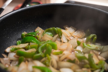 Green peppers and onions cooking with oil in a black pan. Professional cuisine, gourmet asian recipe.