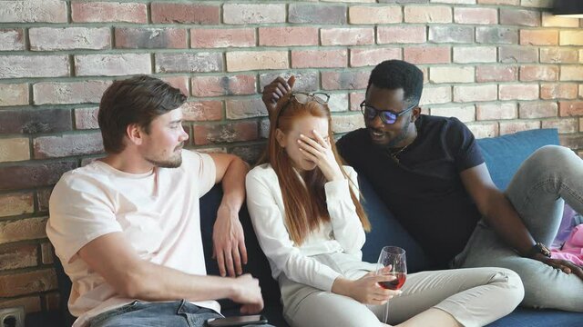 Redhead woman crying sitting on the bed with a glass of champagne among two different men, Threesome concept