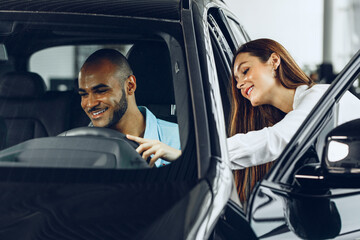 Young woman salesperson in car showroom showing a car to her male client