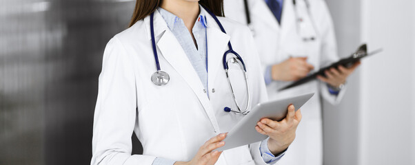 Unknown woman doctor iusing tablet computer in her hands, while standing in clinic. Medicine...