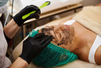 Applying a black charcoal cosmetic mask by a doctor