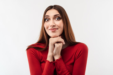 Portrait of brunette dressed in casual red sweater keeping hands together near chin. Studio shot, white background