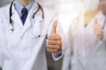 Unknown man-doctor and woman standing straight as a team with thumbs up in sunny clinic. Medicine concept during Coronavirus pandemic. Covid 2019