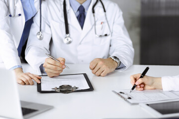 Fototapeta premium Group of unknown doctors are sitting at the desk and discussing problems or disease treatment in modern hospital office. Coronavirus countering, patient help in medicine concept