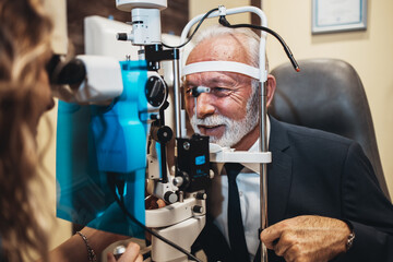 Fototapeta na wymiar Elegant senior bearded man receiving ophthalmology treatment. Doctor ophthalmologist checking his eyesight with modern equipment.