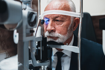 Elegant senior bearded man receiving ophthalmology treatment. Doctor ophthalmologist checking his eyesight with modern equipment.
