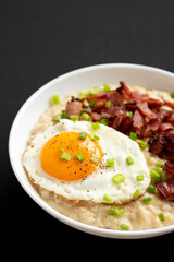 Homemade Cheesy Bacon Savory Oatmeal Bowl on a black background, side view.