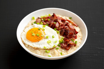 Homemade Cheesy Bacon Savory Oatmeal Bowl on a black surface, side view.